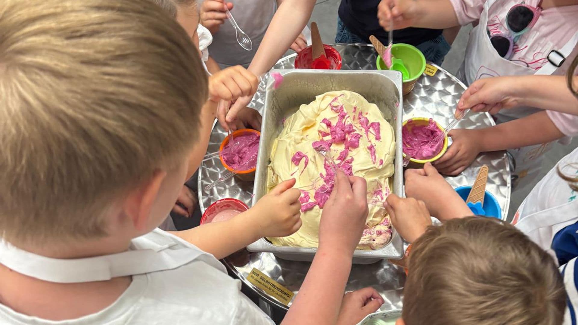 Kinder rühren an einem Metallbecken bunte Eiscreme an